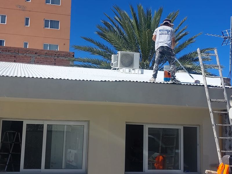 Operario de Sur Aislaciones aplicando un revestimiento blanco con rodillo sobre un techo de chapa